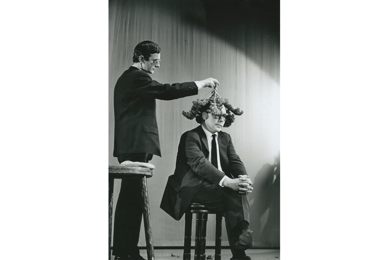 Willem de Ridder dengia Emmetto Williamso galvą kopūsto lapais Robert‘o Filliou performanse 13 Façons d’employer le crâne d’Emmett Williams, Kleine Komedie teatras, Amsterdamas, 1963 m. gruodžio 18 d. Nuotr. Dorine van der Klei