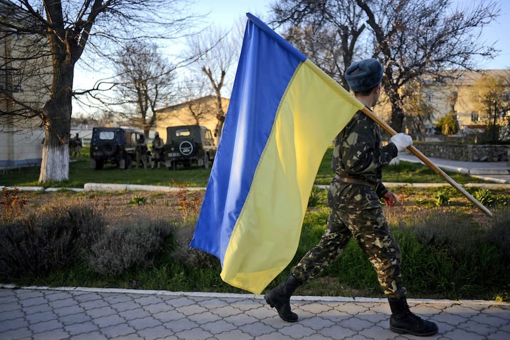 Ukrainiečių karys neša Ukrainos vėliavą Belbeko karinių oro pajėgų bazėje. EPA-Eltos nuotr.