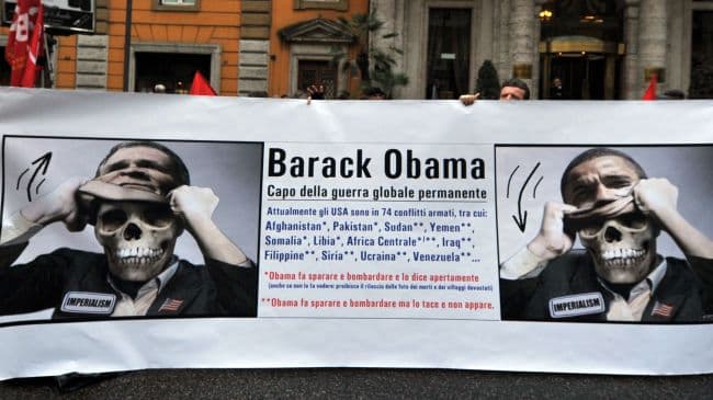 Protestas prie JAV ambasados Romoje kovo 27-ąją. Plakate – užrašas „Barackas Obama – nuolatinio karo vadas“