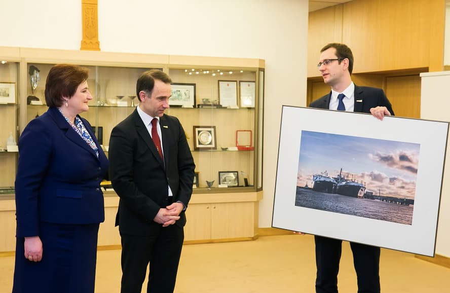 Seimo pirmininkė ir nebaigto terminalo statytojai džiaugiasi „užbaigtu“ projektu ir nupaveiksluotu bei įrėmintu laivo „Independence“ (vokiškai „Unabhängigkeit“) vaizdu.